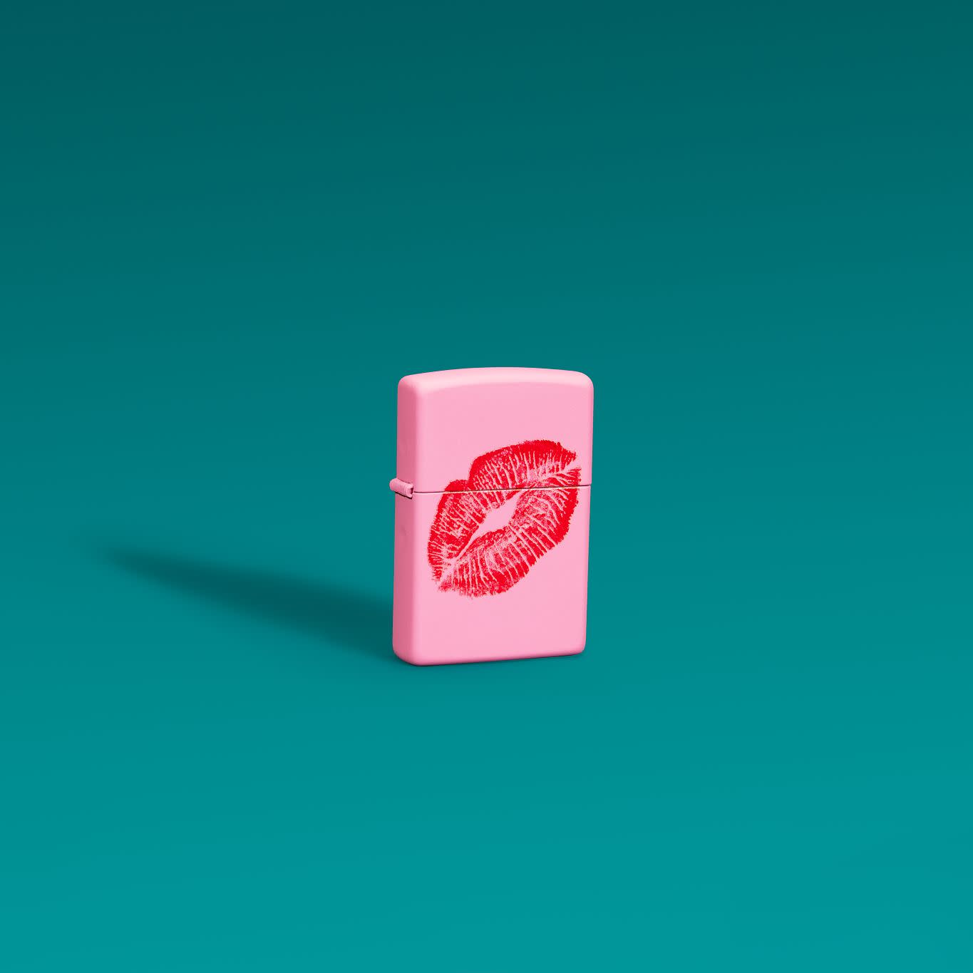 Lifestyle image of Zippo Smooches Design Pink Matte Windproof Lighter standing in front of a teal background.