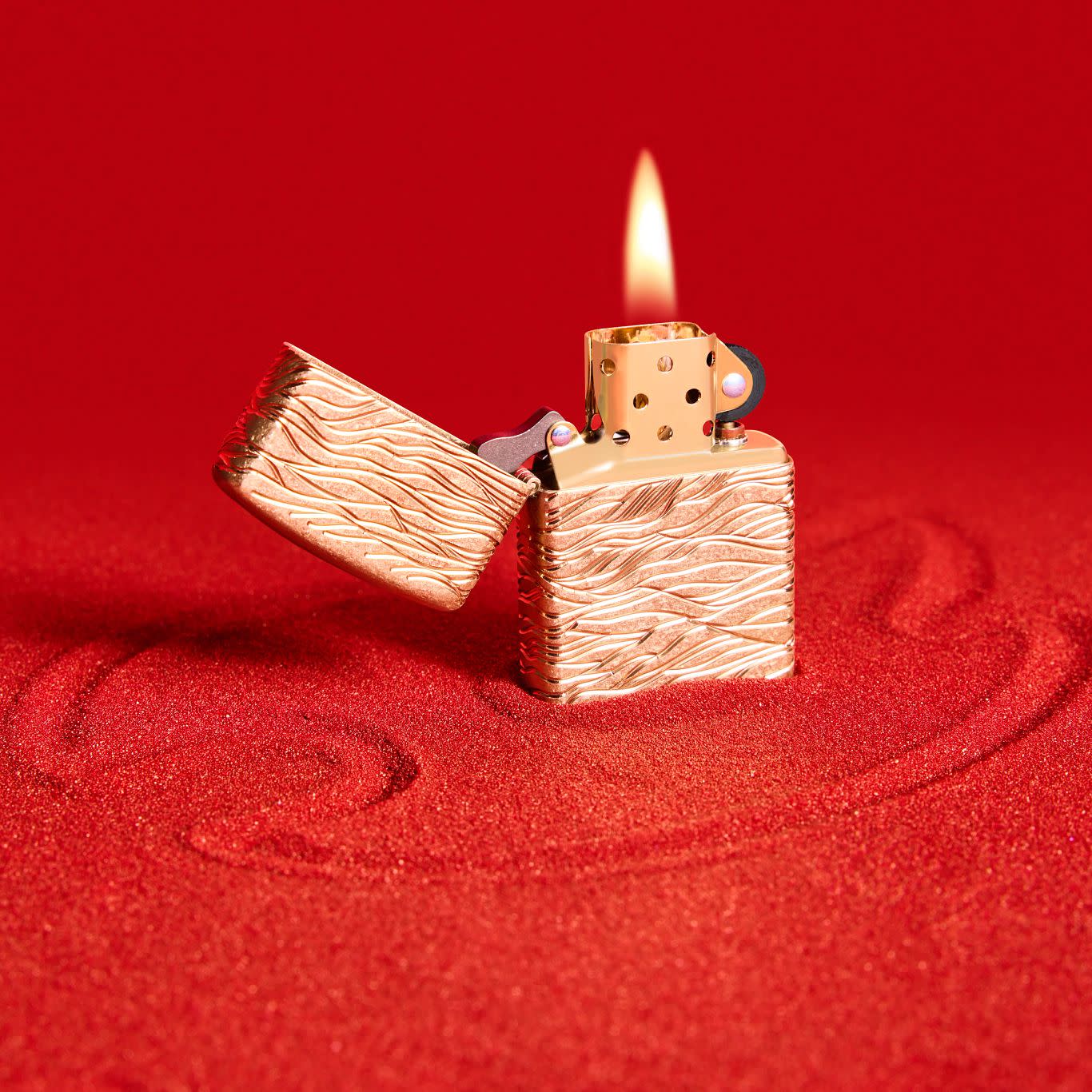 Lifestyle image of Zippo Luxury Waves Design Armor Tumbled Brass Windproof Lighter standing on red sand.