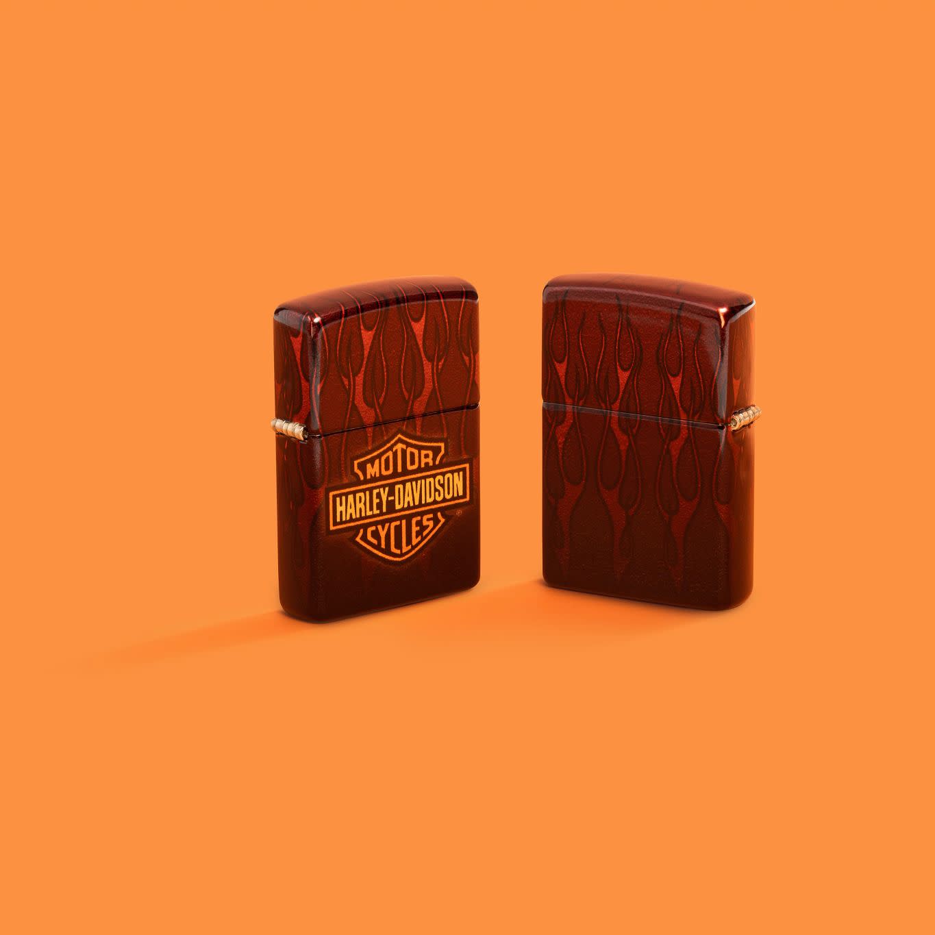 Lifestyle image of two Zippo Harley-Davidson?? 540 Tumbled Brass Windproof Lighters on an orange background.