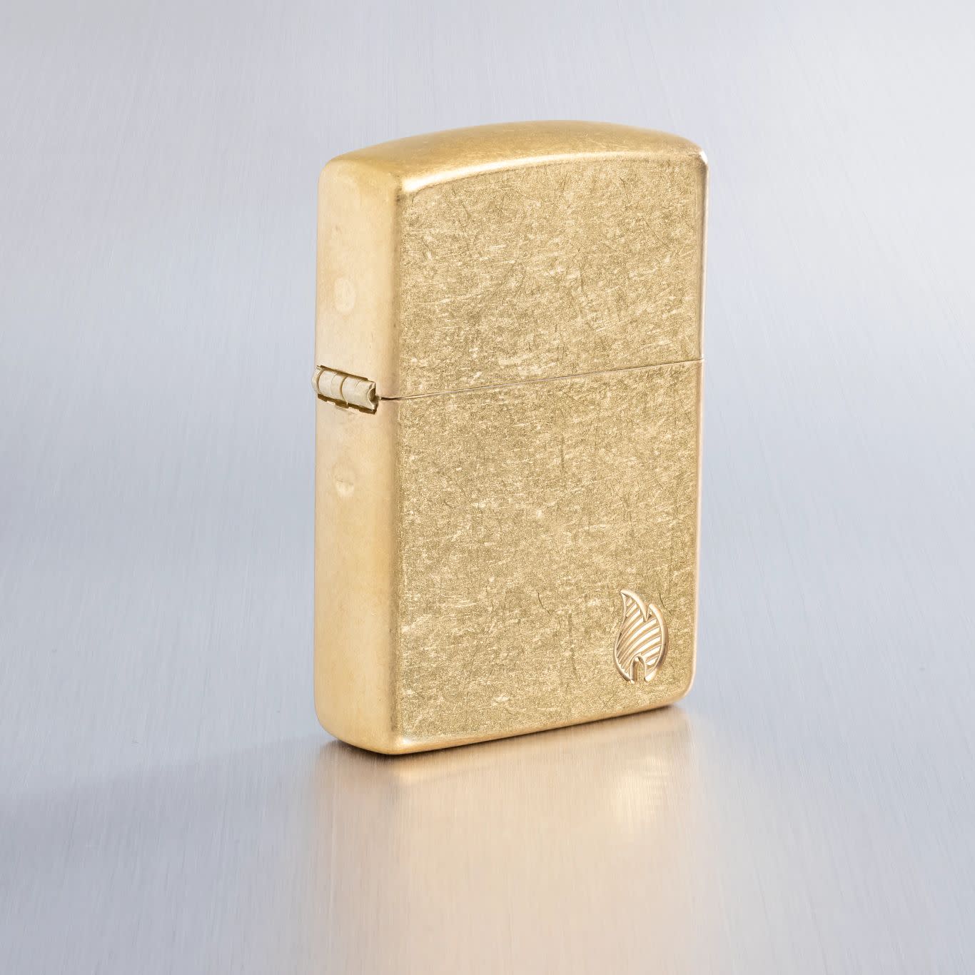 Lifestyle image of Zippo Armor?? Series Flame Tumbled Brass Windproof Lighter on a light gray background.