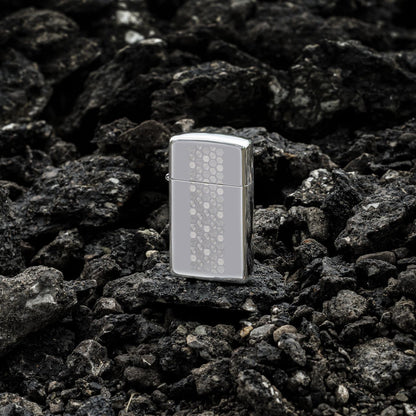 Lifestyle image of Zippo Slim?? Honeycomb Design High Polish Chrome Windproof Lighter standing on dark, loose rocks.