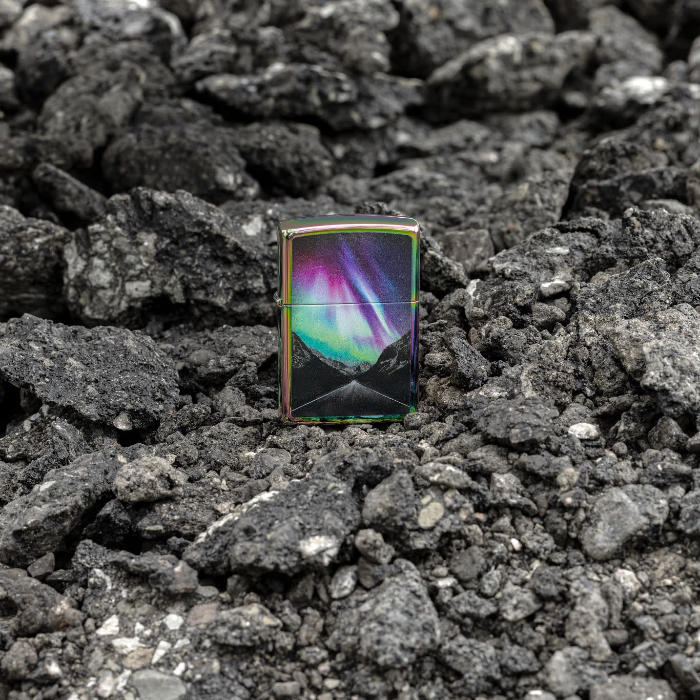 Lifestyle image of Zippo Aurora Road Design Multi Color Windproof Lighter standing on loose rocks.