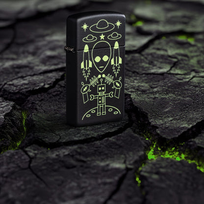 Lifestyle image of Zippo Alien Invasion Design Slim?? Black Matte Windproof Lighter standing on blacktop with green glowing cracks.
