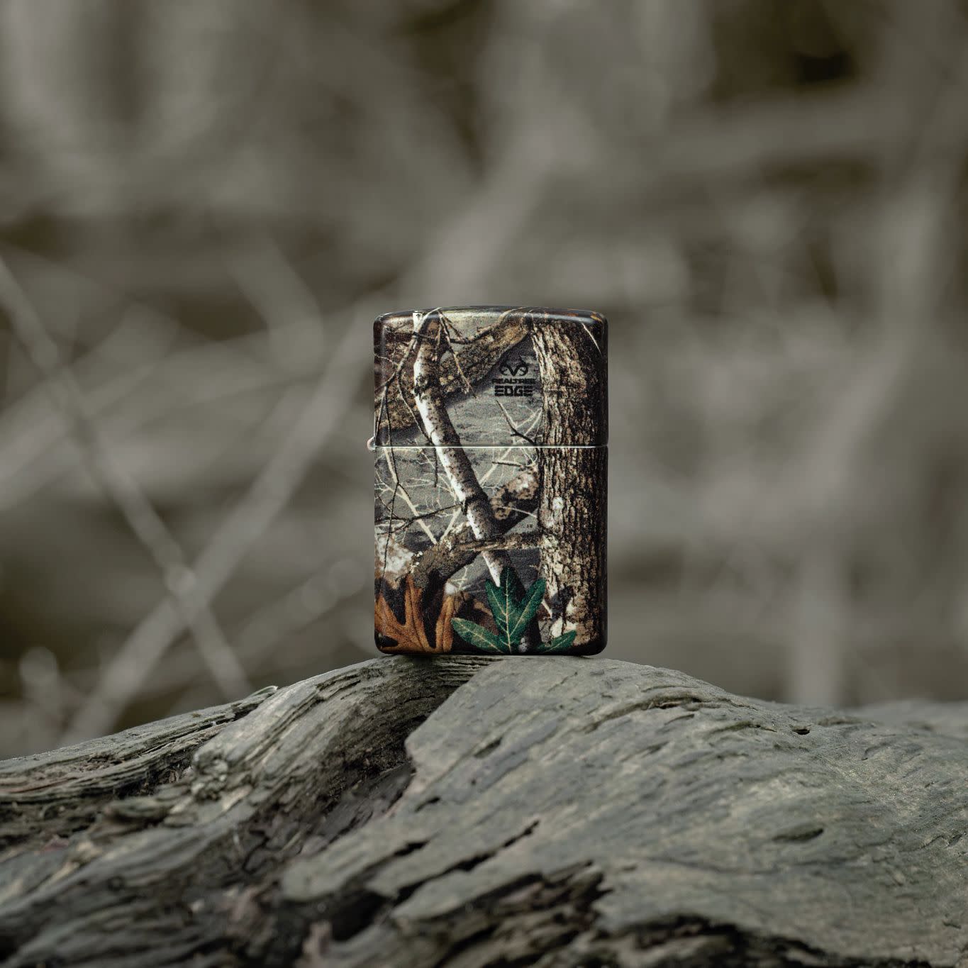 Lifestyle image of Zippo Realtree?? EDGEÆ?âº Camo Design 540 Matte Windproof Lighter standing on a fallen limb in a wooded scene.