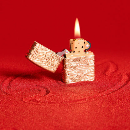 Lifestyle image of Zippo Luxury Waves Design Armor Tumbled Brass Windproof Lighter standing on red sand.