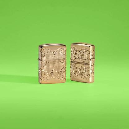 Lifestyle image of two Zippo Lucky Clover Design Armor?? High Polish Gold Plate Windproof Lighters in a lime green scene, one showing the front of the lighter and the other showing the back.