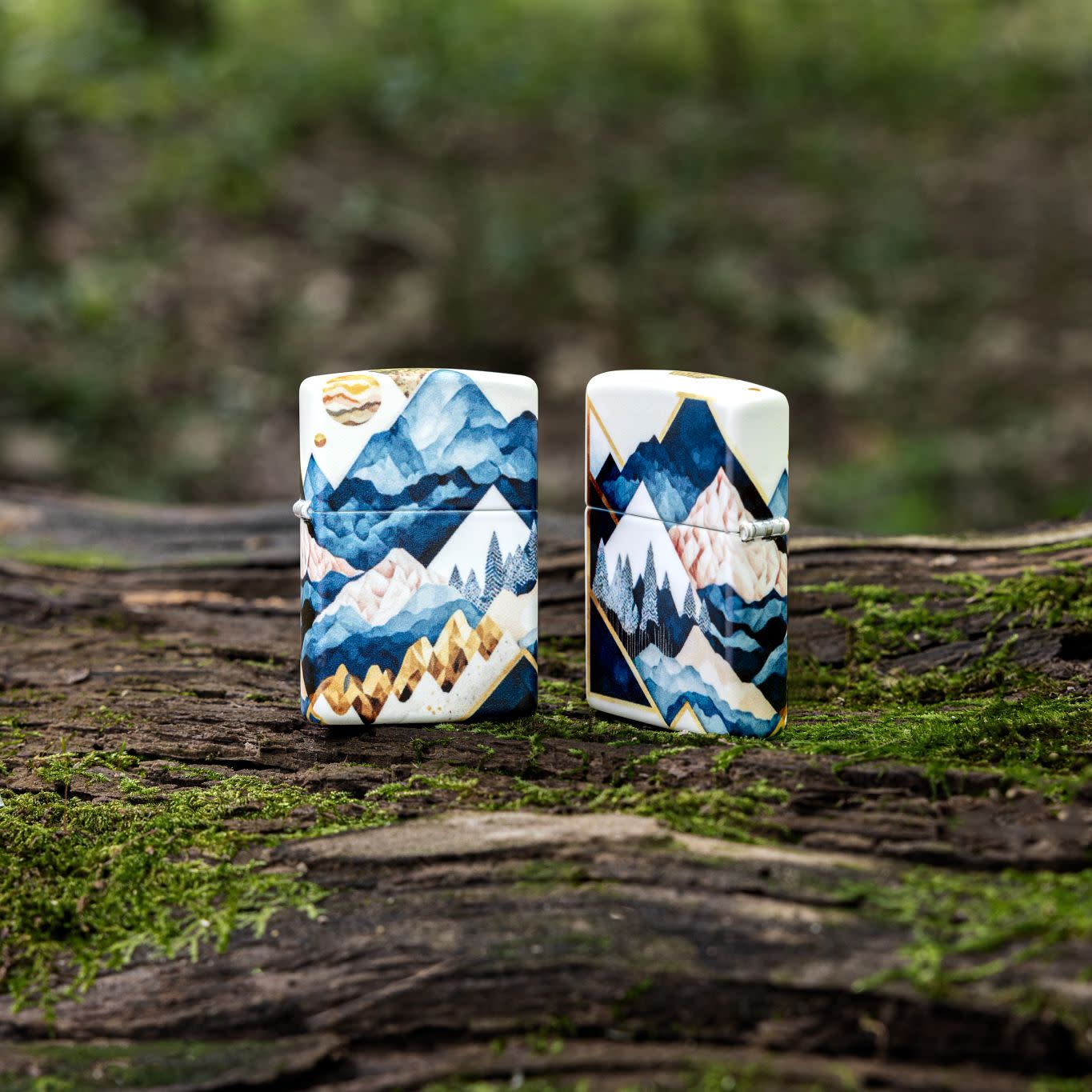 Lifestyle image of two Zippo Mountain Collage Design 540 Matte Windproof Lighters standing on a mossy log, one showing the front of the lighter and one showing the back.